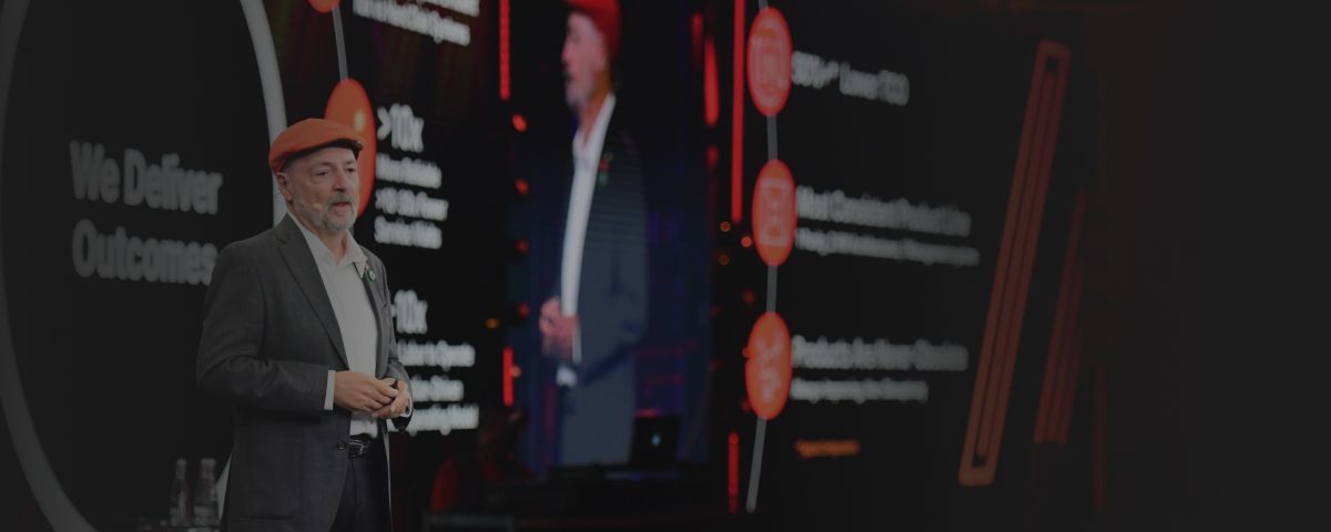 Presenter at a conference sharing insights with a visual display in the background