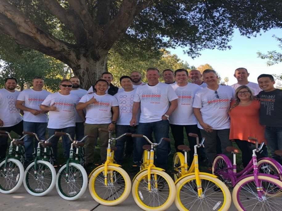 Groupe de personnes prenant la pose en souriant, avec des bicyclettes de différentes couleurs